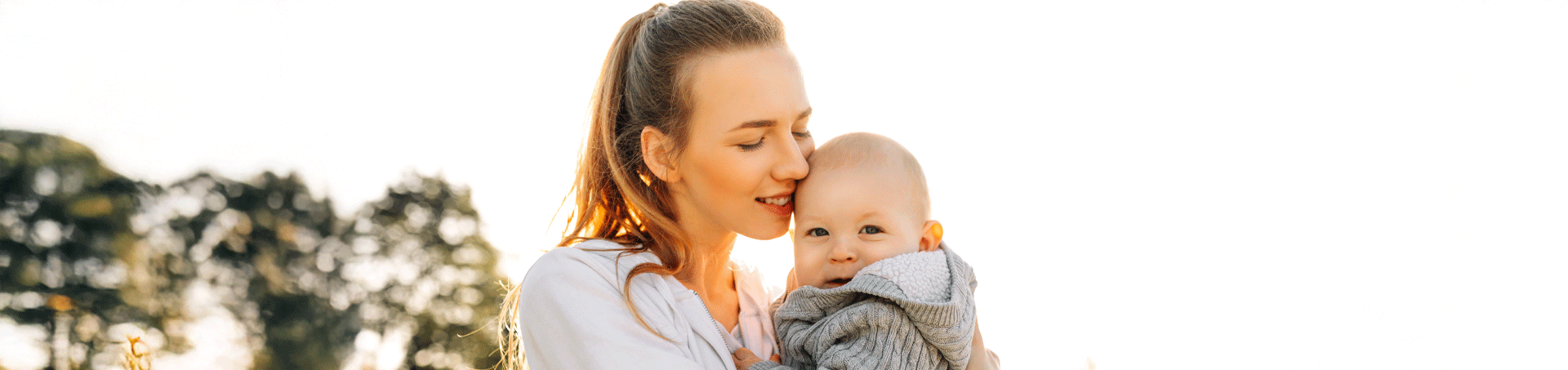 mother holder her baby outside with the sun behind them