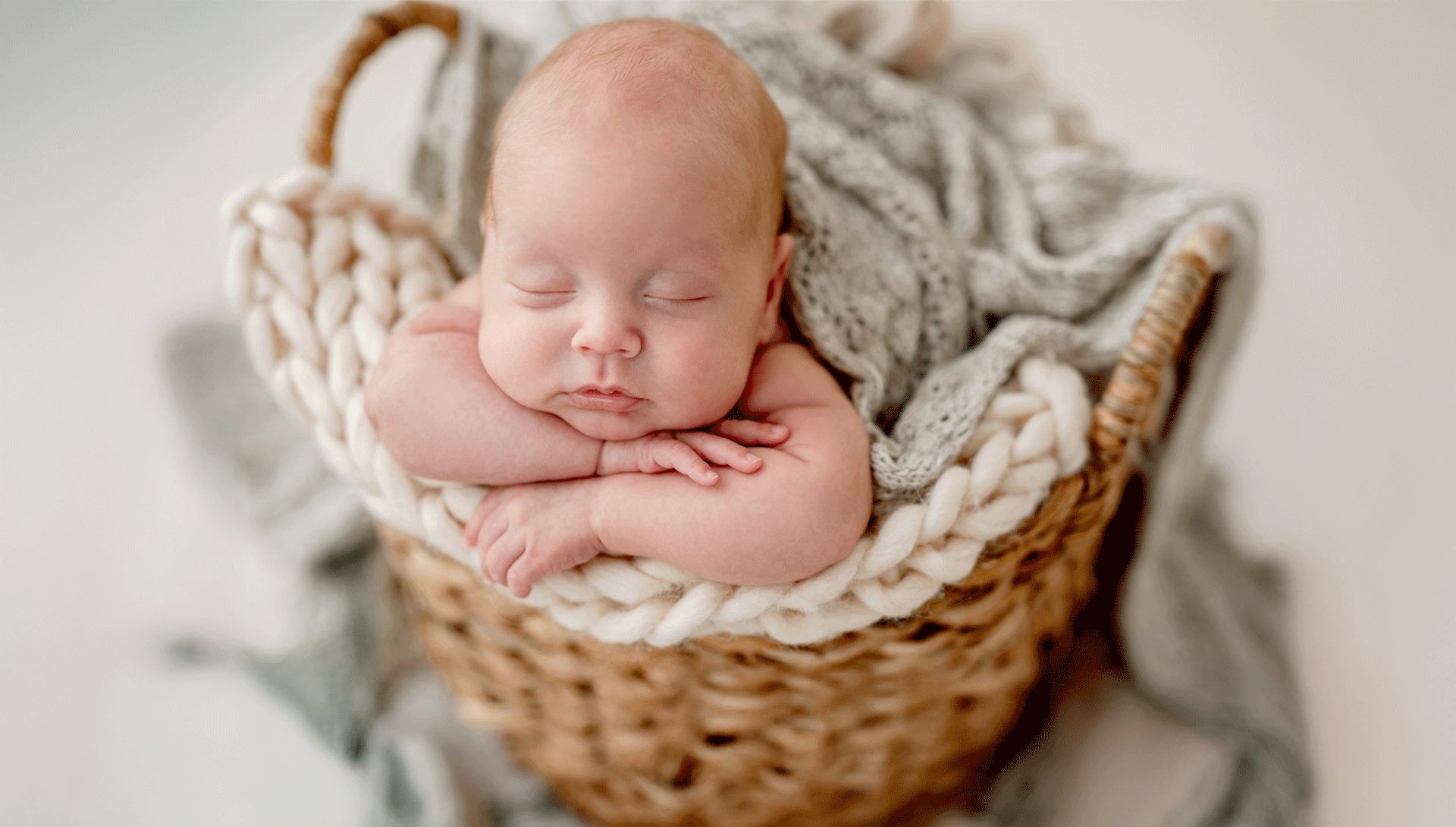 newborn baby nestled in a knit blanket in a basket
